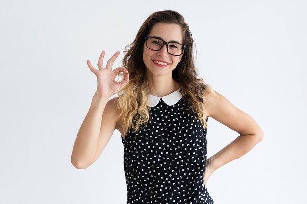 Giovane bella donna sorridente che mostra segno GIUSTO e che esamina macchina fotografica.