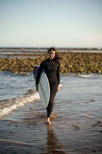 Giovane bella donna surfista sulla spiaggia al tramonto