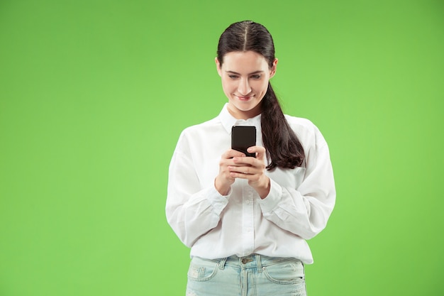 Giovane bella donna utilizzando il telefono cellulare sulla parete di colore verde. Concetto di emozioni facciali umane.