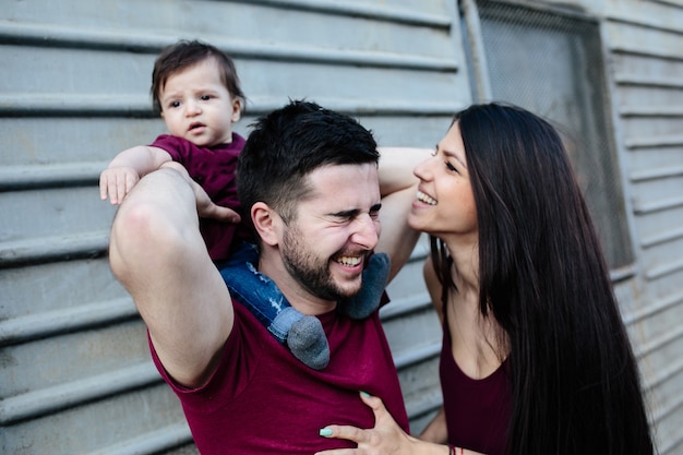 Giovane bella famiglia con bambino in posa sul muro grigio