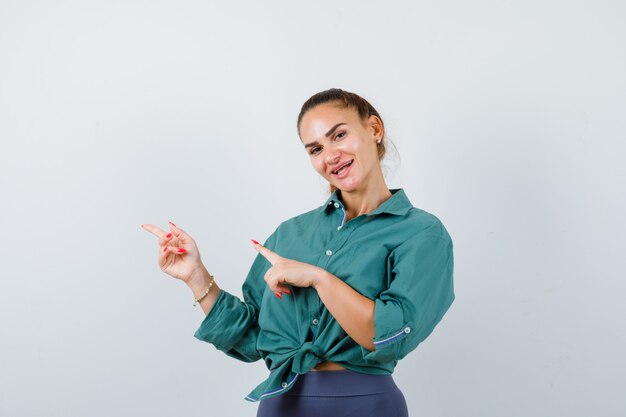 Giovane bella femmina che punta a sinistra in camicia verde e sembra allegra. vista frontale.