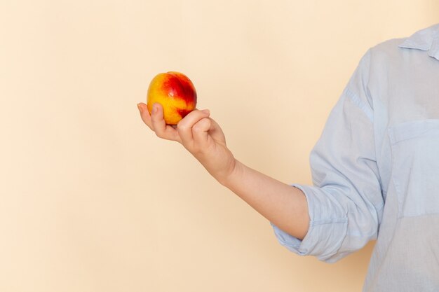 Giovane bella femmina di vista frontale in camicia che tiene mela sulla posa della donna del modello della frutta della parete crema