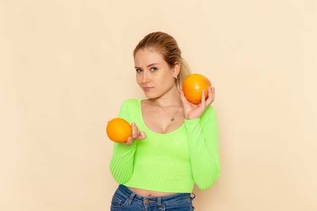 Giovane bella femmina di vista frontale in camicia verde che tiene le arance morbide fresche sulla donna di modello della frutta crema della parete mellow