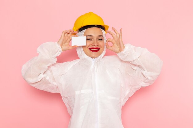 giovane bella femmina in abito bianco speciale e casco giallo che tiene scheda bianca