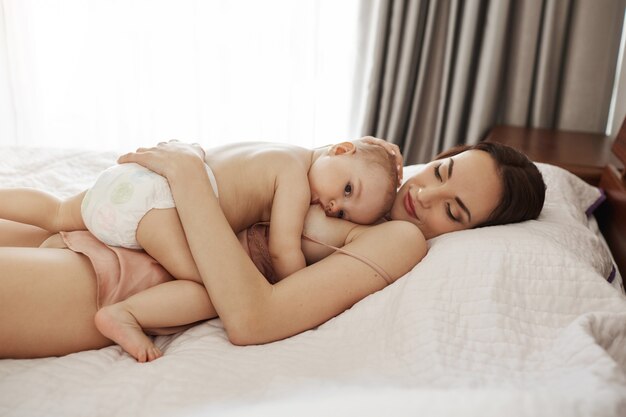 Giovane bella mamma felice l'allattamento al seno che abbraccia il suo bambino sdraiato sul letto a casa.