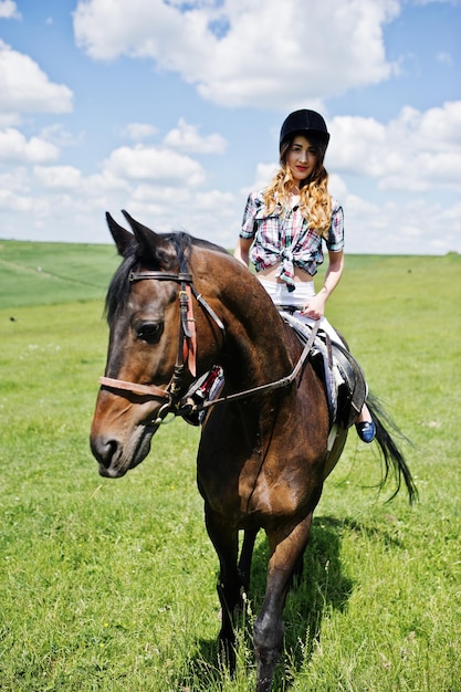 Giovane bella ragazza a cavallo su un campo in una giornata di sole