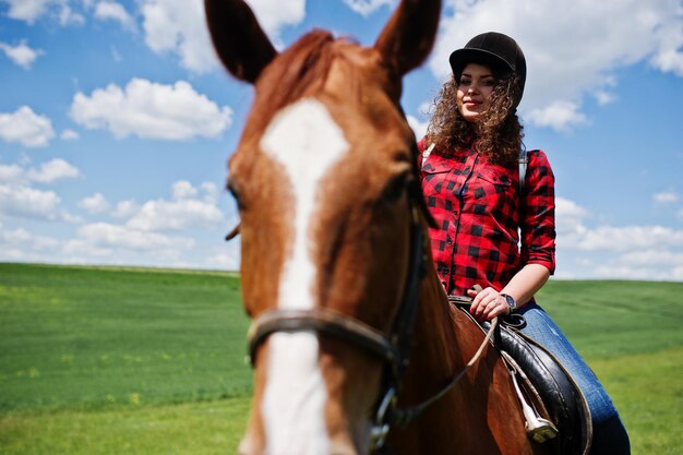 Giovane bella ragazza a cavallo su un campo in una giornata di sole