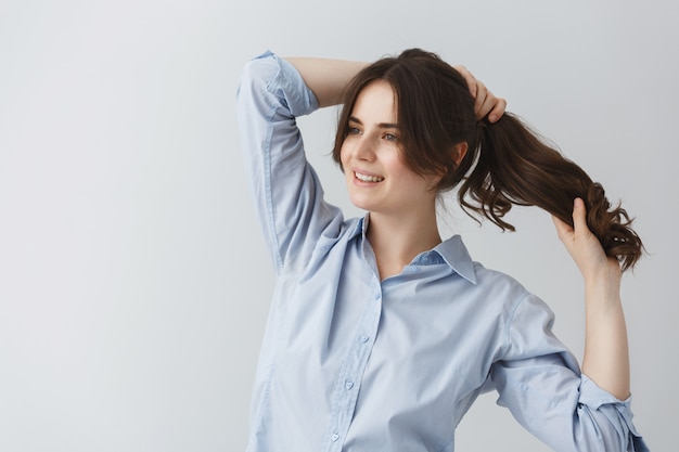 Giovane bella ragazza caucasica che fa acconciatura, preparandosi per uscire la mattina presto con l'espressione del viso felice.