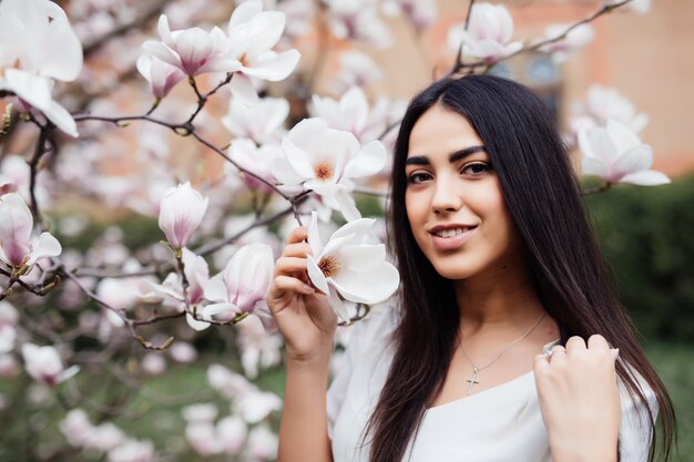 Giovane bella ragazza caucasica in un giardino fiorito di magnolia primavera. La ragazza al mattino in giardino. Ritratto, primo piano.