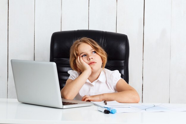 Giovane bella ragazza che si siede al posto di lavoro in ufficio.