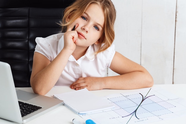 Giovane bella ragazza che si siede al posto di lavoro in ufficio.