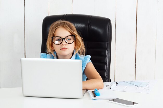 Giovane bella ragazza che si siede al posto di lavoro in ufficio.