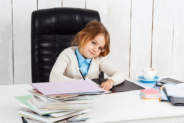 Giovane bella ragazza che si siede al posto di lavoro in ufficio.