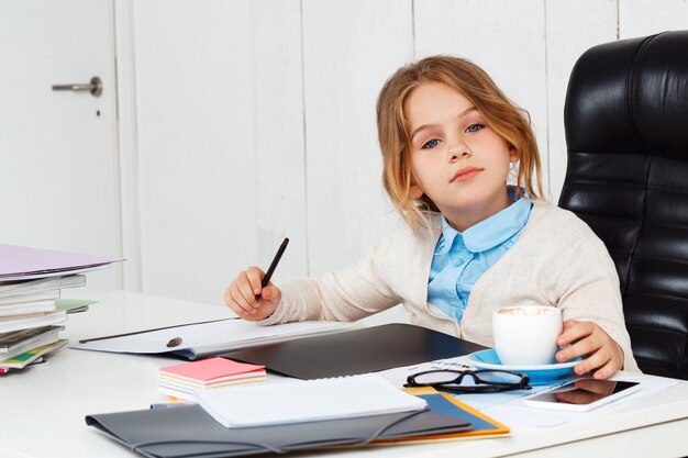 Giovane bella ragazza che si siede al posto di lavoro in ufficio.