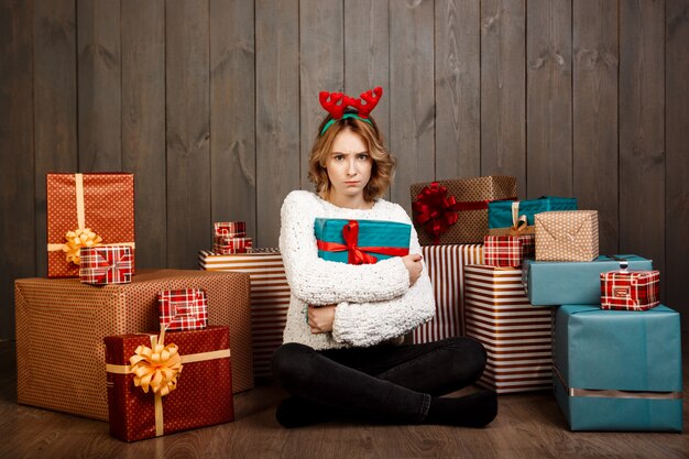 Giovane bella ragazza che si siede fra i regali di natale sopra la parete di legno