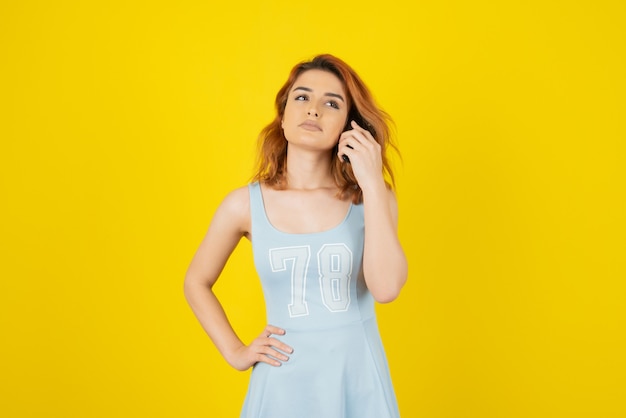 Giovane bella ragazza con abito blu su giallo.