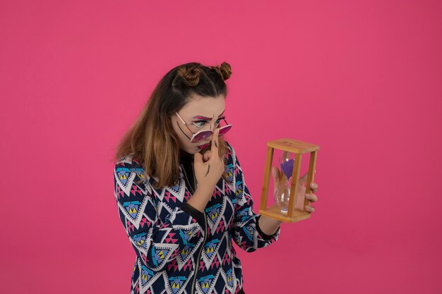 Giovane bella ragazza con orologio di sabbia e occhiali che guardano a lato. Foto di alta qualità