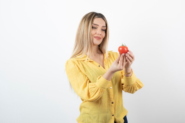 Giovane bella ragazza in camicia gialla guardando pomodoro rosso su bianco.