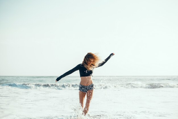 giovane bella ragazza in posa sulla spiaggia, oceano, onde, sole splendente e pelle abbronzata