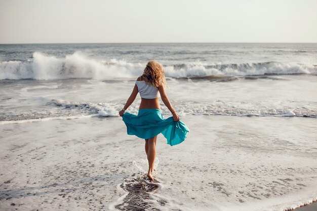 giovane bella ragazza in posa sulla spiaggia, oceano, onde, sole splendente e pelle abbronzata