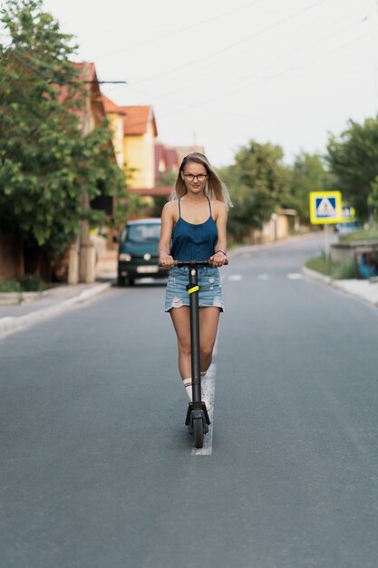 Giovane bella ragazza in sella a uno scooter elettrico in estate sulla strada