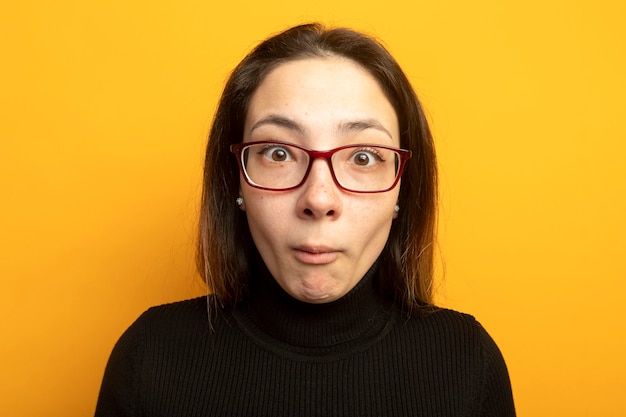Giovane bella ragazza in un dolcevita nero confuso e sorpreso