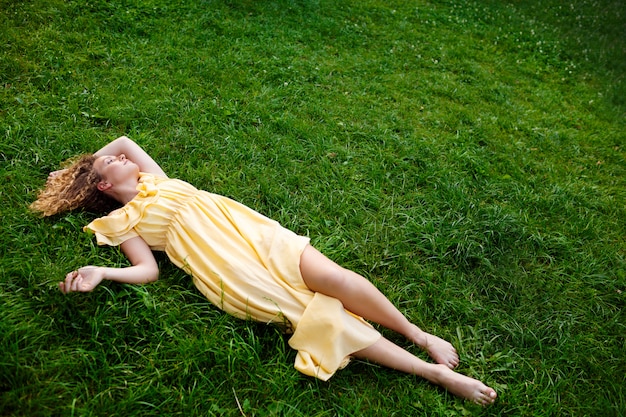 Giovane bella ragazza in vestito giallo che si trova sull'erba.