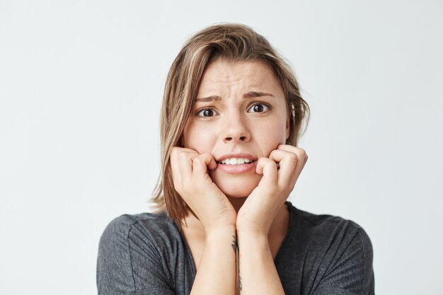 Giovane bella ragazza nervosa che si tiene per mano sulle guance.