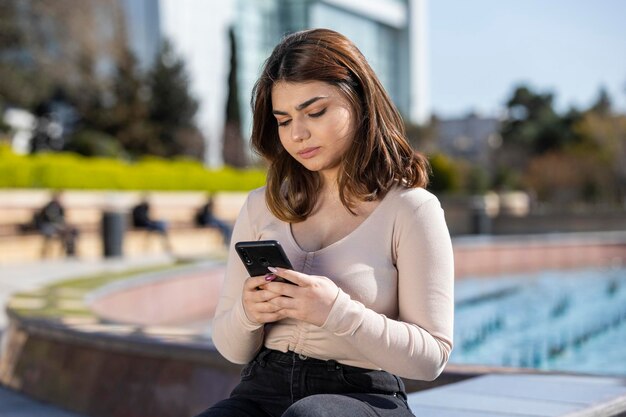 Giovane bella ragazza premurosa che esamina il suo telefono Foto di alta qualità