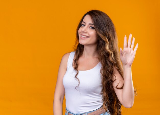 Giovane bella ragazza sorridente che gesturing ciao sullo spazio arancione isolato con lo spazio della copia