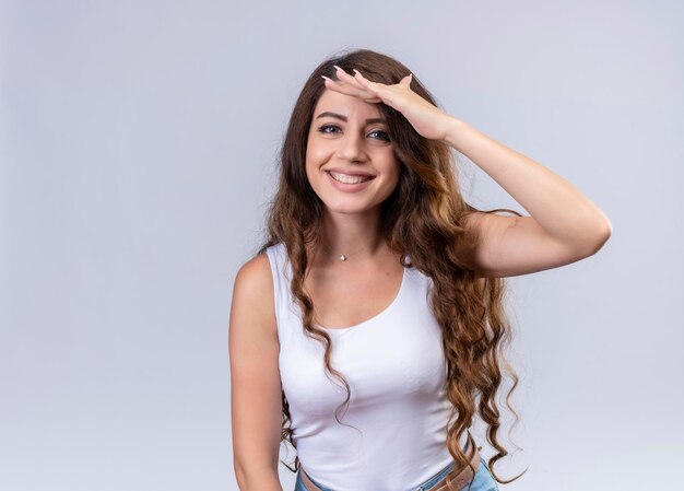 Giovane bella ragazza sorridente che mette la mano sulla fronte che esamina la distanza con lo spazio della copia