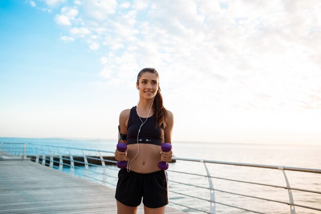 Giovane bella ragazza sportiva che si prepara all'alba sulla spiaggia.