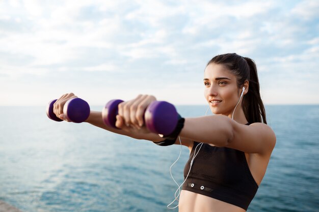 Giovane bella ragazza sportiva che si prepara all'alba sulla spiaggia.