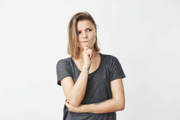 Giovane bella ragazza vaga che pensa con la mano sul mento che guarda in aggrottare le sopracciglia laterale.