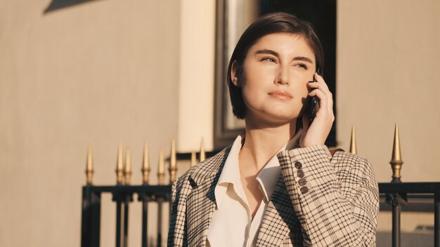 Giovane bella signora che parla su smartphone in attesa di affari si incontrano sulla strada della città. Sempre in contatto