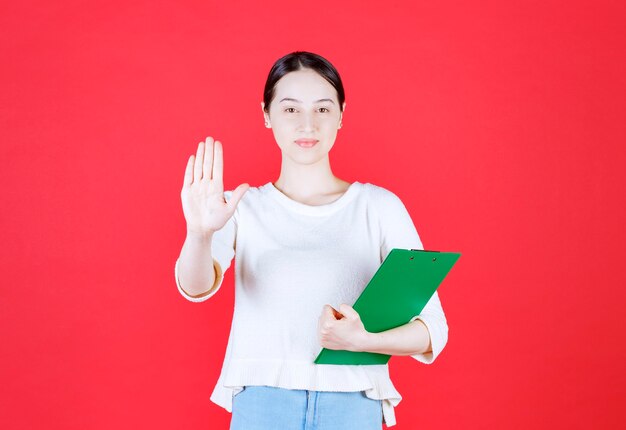 Giovane bella signora in possesso di appunti e gesticolando stop