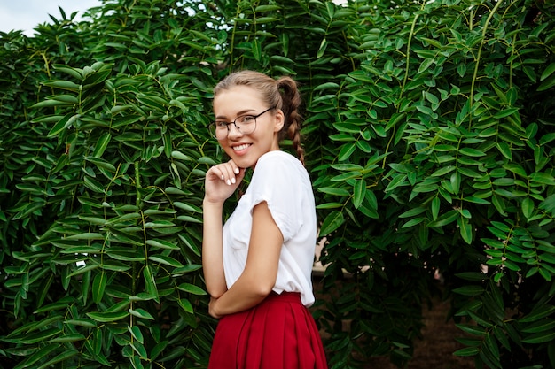 Giovane bella studentessa in vetri che sorride, posando sopra le foglie all'aperto.