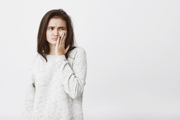 giovane bellissimo modello femminile con i capelli castani, tenendo il palmo sulla guancia, esprimendo infelicità, stanchezza e frustrazione