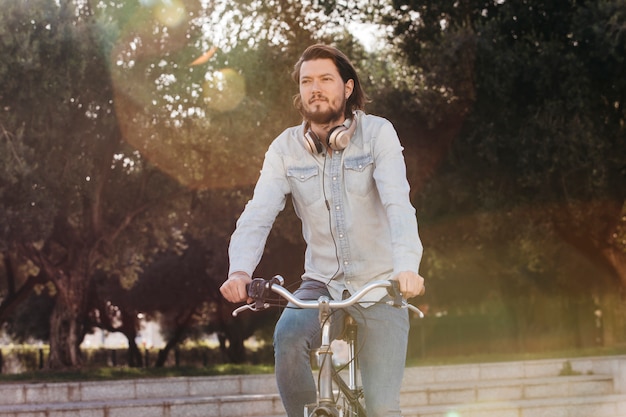 Giovane bello che guida la sua bicicletta nel parco