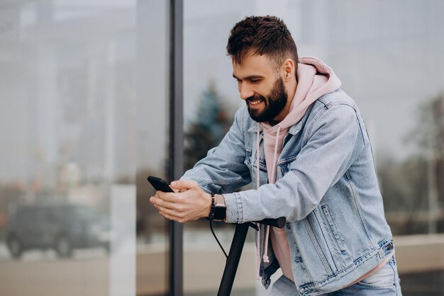 Giovane bello che guida uno scooter elettrico e utilizza il telefono