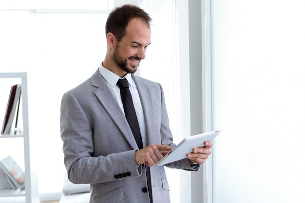 Giovane bello che lavora con la compressa digitale nell&#39;ufficio.