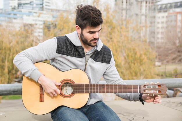 Giovane bello che si siede nel parco che gioca chitarra