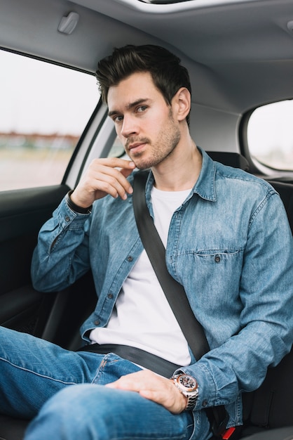 Giovane bello che si siede nel seggiolino auto guardando la fotocamera