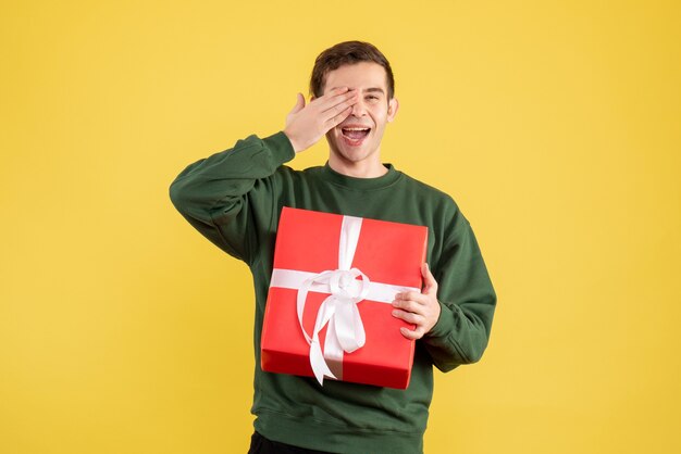 Giovane bello di vista frontale con il maglione verde che sta sul colore giallo