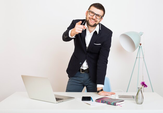 Giovane bello elegante hipster uomo in giacca nera al tavolo da ufficio, stile aziendale, camicia bianca, isolato, lavorando su laptop, avvio, posto di lavoro, dito puntato, sorridente, felice, positivo,