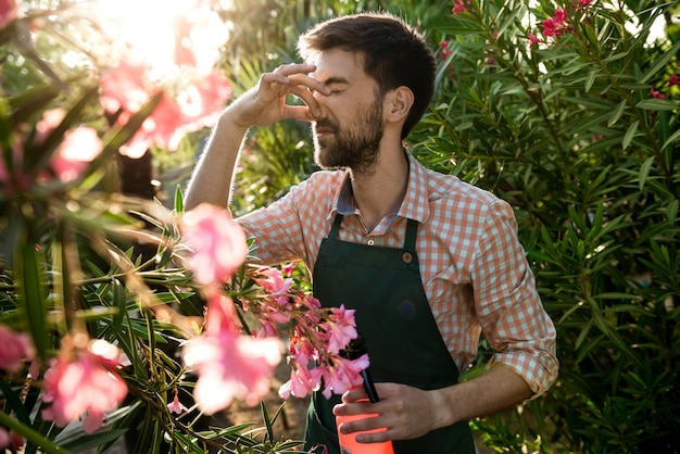 Giovane bello giardiniere allegro che copre il naso dall'odore con le dita