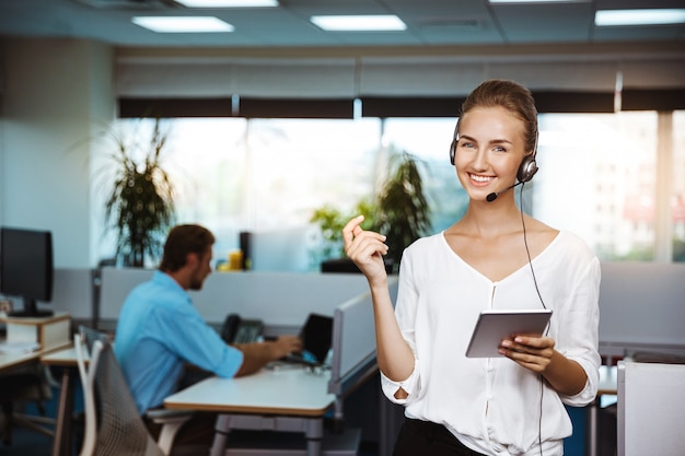 Giovane bello operatore telefonico femminile di sostegno che parla, consultando, sopra l'ufficio