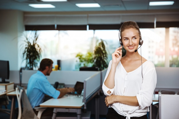 Giovane bello operatore telefonico femminile di sostegno che parla, consultando, sopra l'ufficio