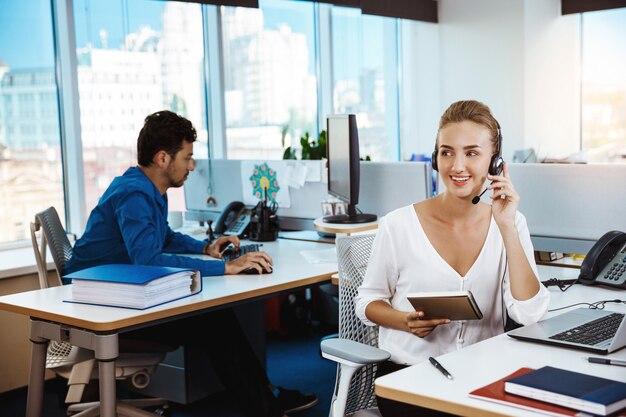 Giovane bello operatore telefonico femminile di sostegno che parla, consultando, sopra l'ufficio