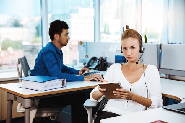 Giovane bello operatore telefonico femminile di sostegno che parla, consultando, sopra l'ufficio